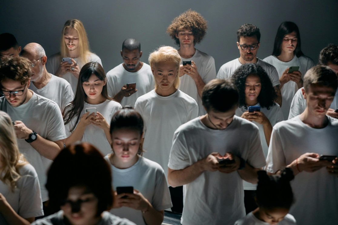 A group of diverse people, all dressed in white t-shirts, are focused on their smartphones, illustrating how digital overload fuels addictive behaviors