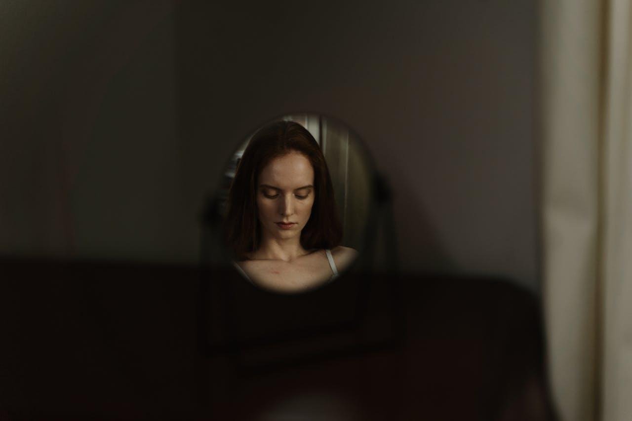 Woman looking down in the mirror with sadness